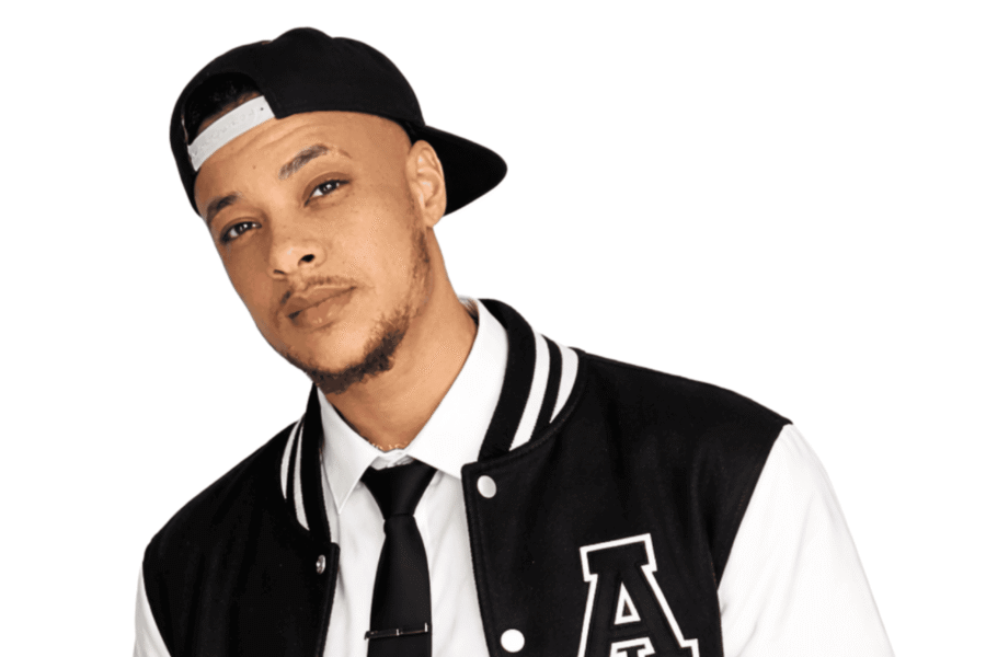 Photo of Nate Ethan on a white background. Nate wears a backward back baseball cap, white shirt and black tie and a varsity sports jacket in black with white sleeves and the letter A embossed on the left chest