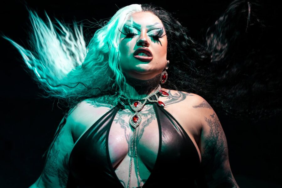 An edgy picture as AfterShock is lit in a minty blue light, their hair is mid air and their tattoos are on show.