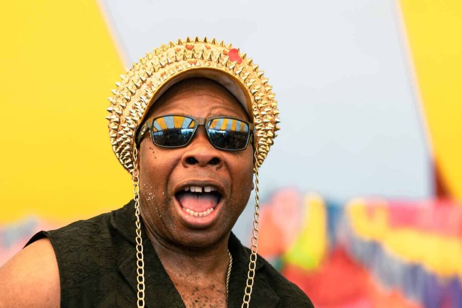 Edson looks very happy as they stare at the camera with their sunglasses and their gold studded hat.