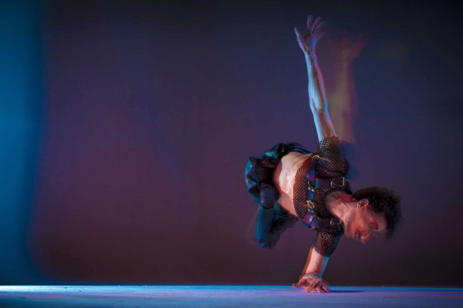 a motion shot of Jonny doing a one handed hand stand on their side their other arm in the air in a blurred wave