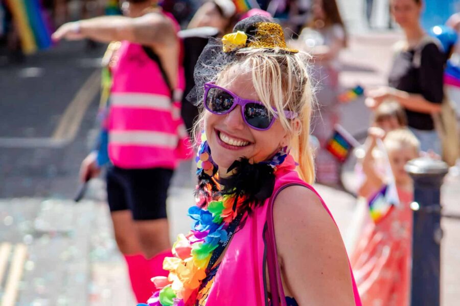 A parade volunteer in sunglasses smiles and is wearing a pink Hi vis jacket