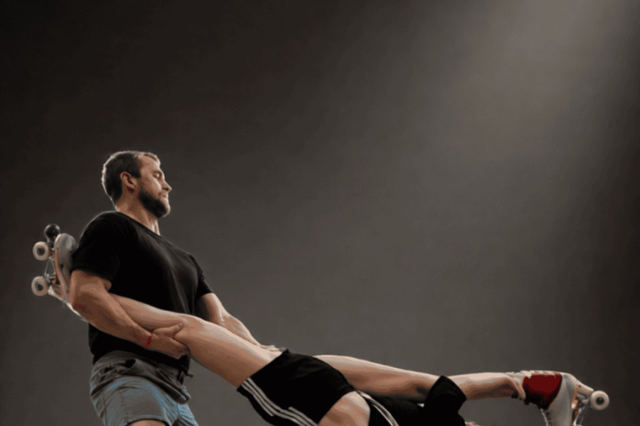 Two performers mid roller skate routine, one holds the others legs as they swing out mid air.