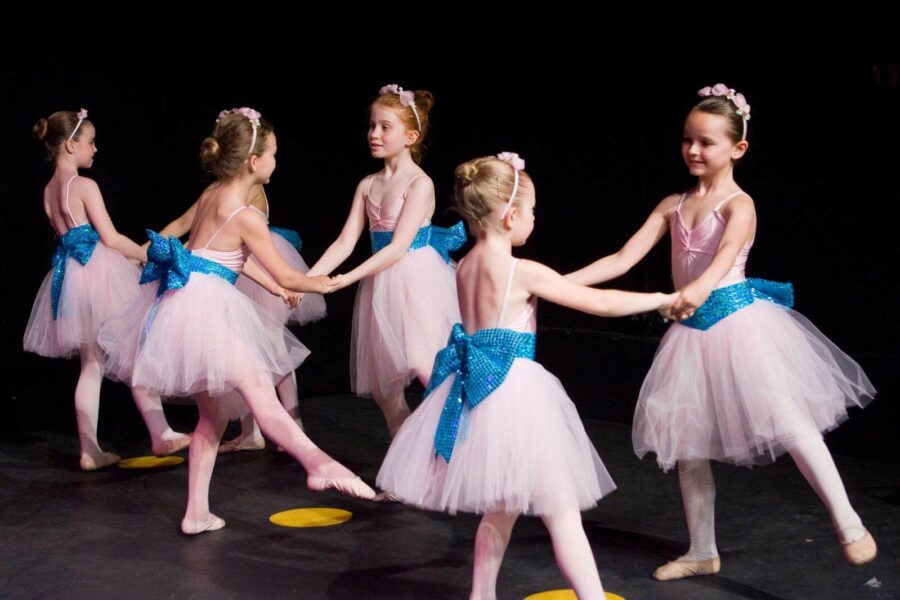 Young dancers in big white tutus with blue bows round the waist. There are three pairs mid movement.