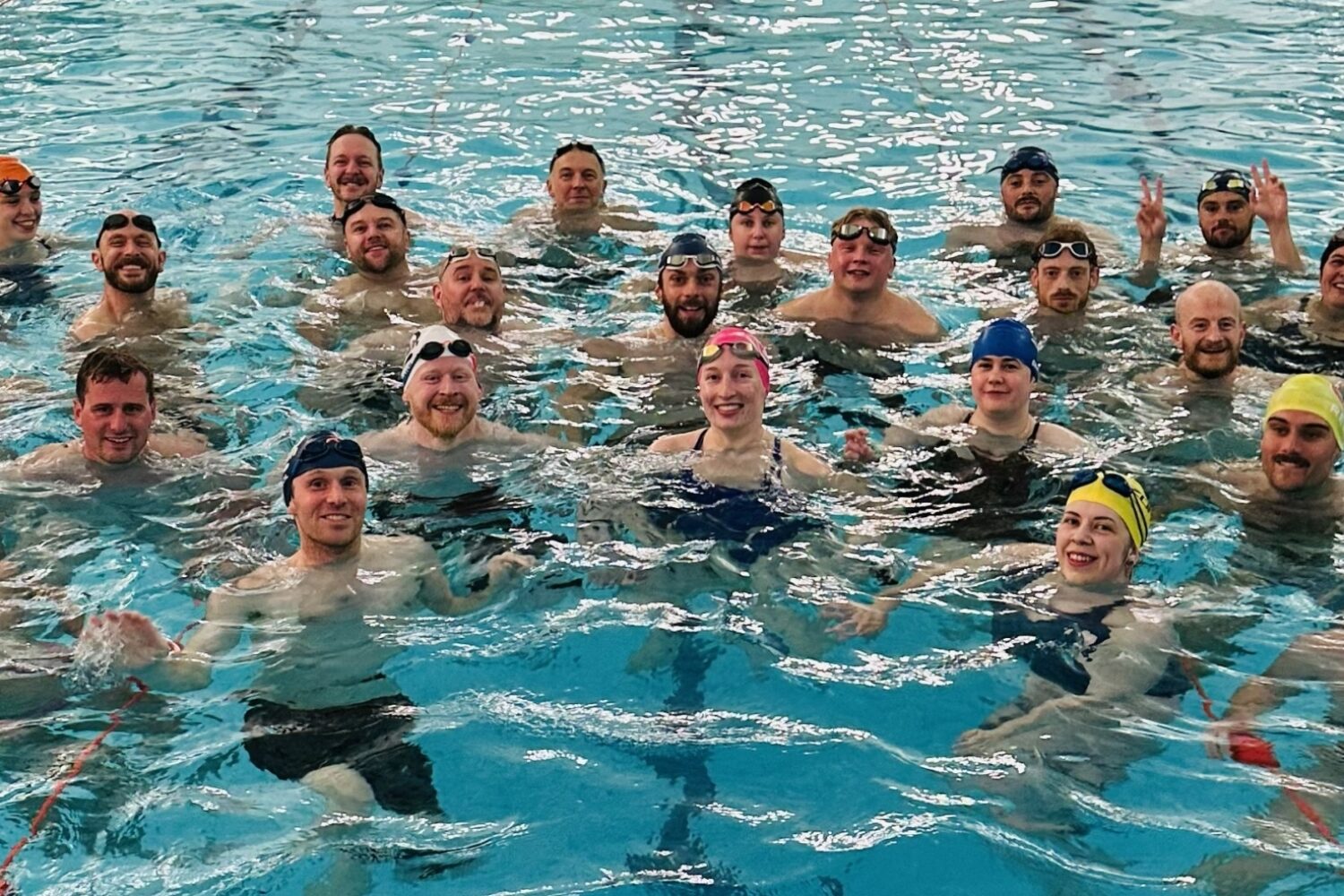 A group of people in a pool, they are looking at the camera and smiling, they are wearing swimcaps and treading water.