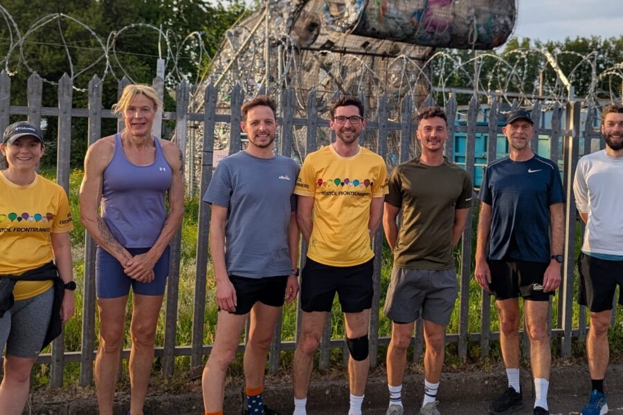 A group of runners stood outside, they are smiling at the camera.