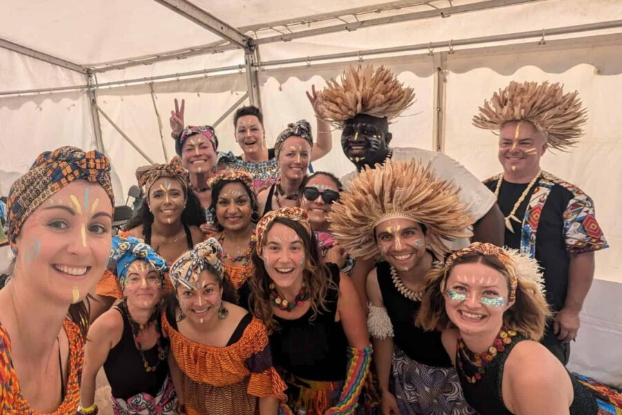 A group smiling for a photo, they are wearing headreses made of feathers, and have designs painted on their face.