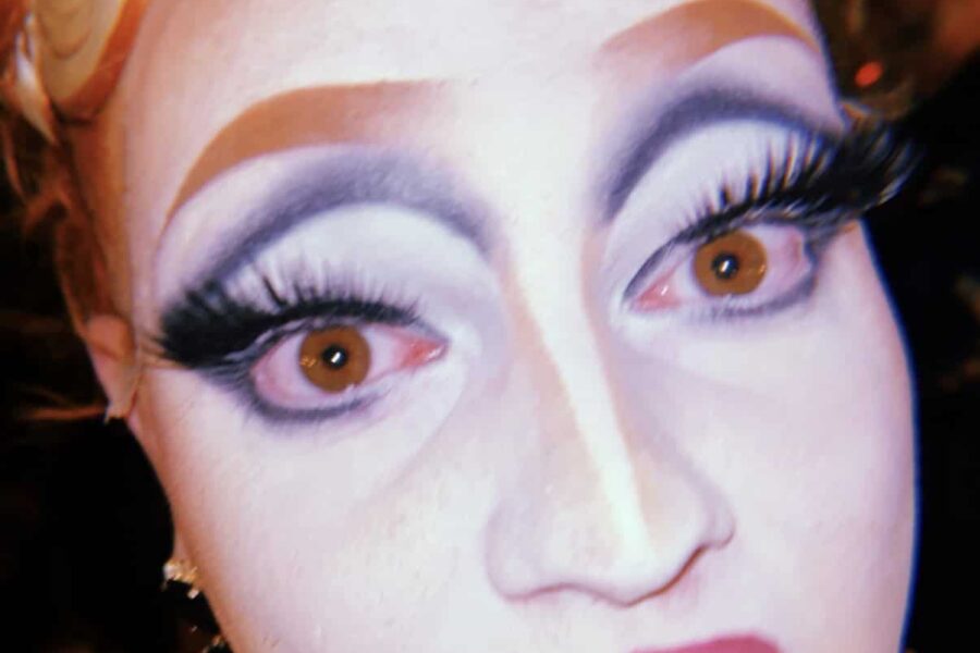 A close up of a pale painted face with huge lashes and a disoriented expression.