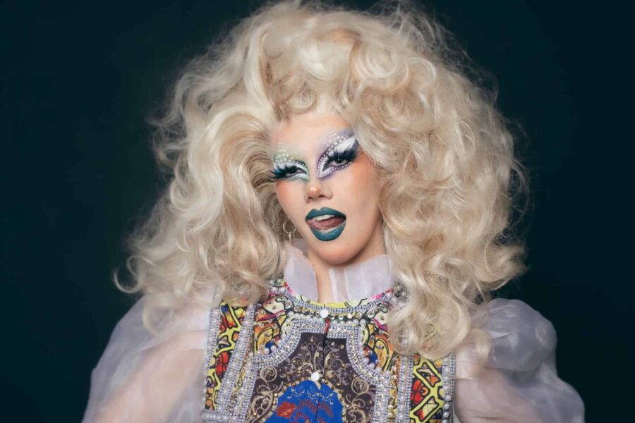 Xanthe is made up beautifully in a huge cascading blonge wig, her makeup is blueish and has pearls dotted over it. Her tounge is caught mid way through running over her teeth giving the picture a cheeky, daring expression.
